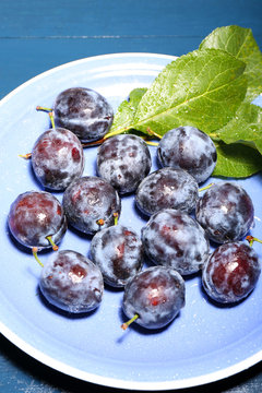 Ripe sweet plums on blue plate, on wooden table