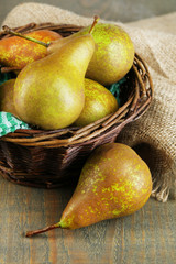 Ripe pears in wicker basket, on wooden background