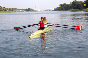 Two young girls in a boat, paddles on the tranquil lake