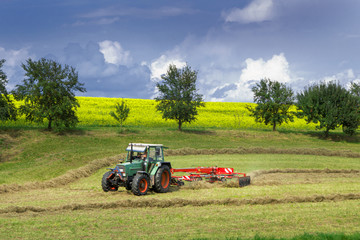 Traktor mit Heuwender vor einem Rapsfeld