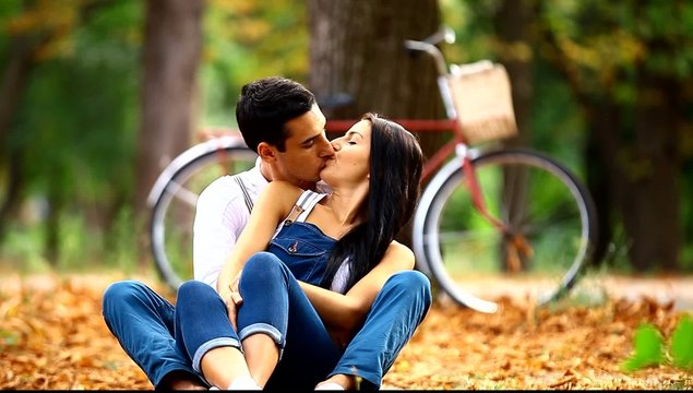 Teen couple with retro bike kissing in the park in autumn time