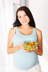 Pregnant woman eating a salad smiling