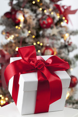 Päckchen mit Schleife vor geschmücktem Weihnachtsbaum