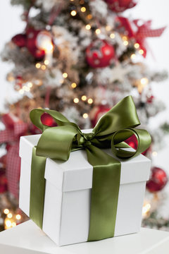 Päckchen mit Schleife vor geschmücktem Weihnachtsbaum