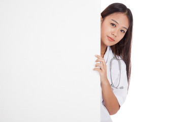 Young Asian female doctor peeking from behind blank sign billboa