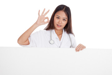Fototapeta premium Young Asian female doctor show OK sign behind blank white billb