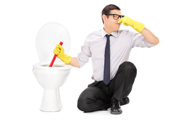 Young man unclogging a stinky toilet with plunger