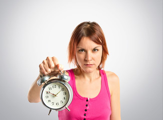 Serious redhead girl holding a clock over white background