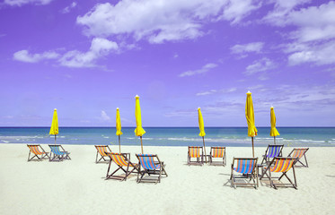Lots of beach chairs and closed umbrellas on white sand beach.