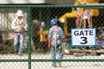 Workers in construction site, focus on chain link fence.
