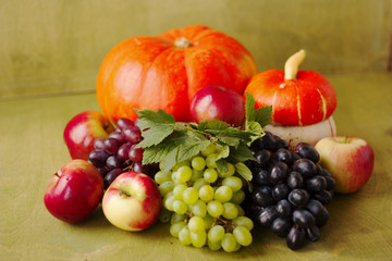 one pumpkin, apples, grapes on a green wooden background