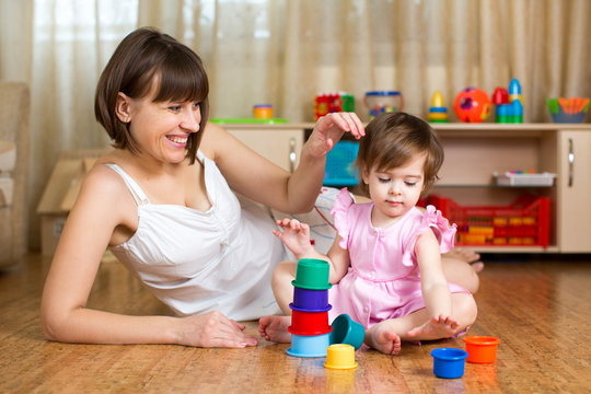 kid girl and mother play together with cup toys