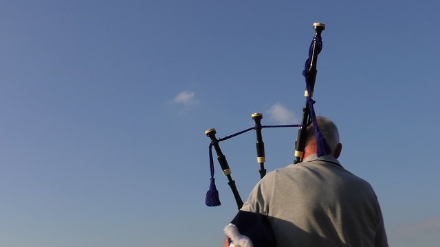Rear view of an old man playing bagpipes isolated