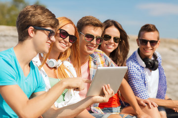 group of smiling friends with tablet pc outdoors