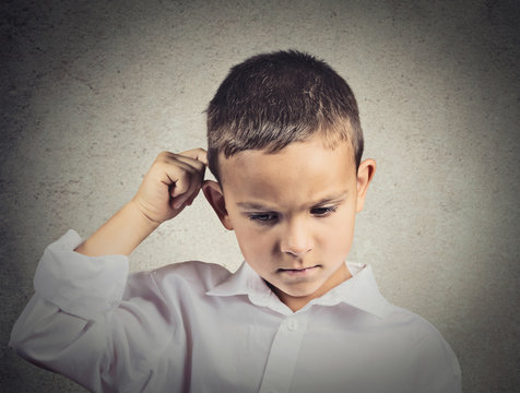 Thinking sad child, scratching back of his head, grey background