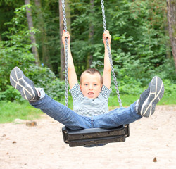 Hilarious boy have a fun on a garden swing.