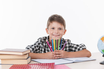 cute boy sitting at table and holding colorful pencils.