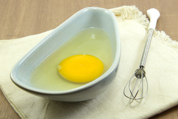 Raw egg in bowl with whisk on cloth
