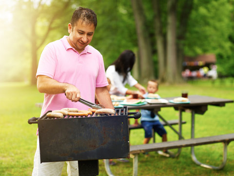 father grilling hot dogs and bratwurst for family at barbecue