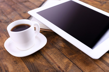 Tablet, cup of coffee and notebook on wooden background