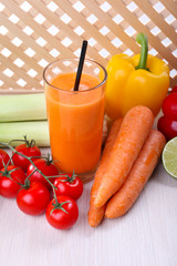 Glass of fresh carrot juice and vegetables on wooden table