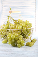 Ripe grapes in metal basket on wooden table on light background