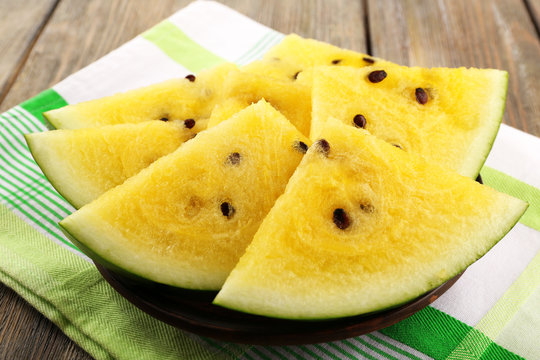 Slices of yellow watermelon on napkin on wooden background