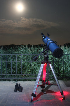 Amateur telescope in a public park pointing at moon on starry sky