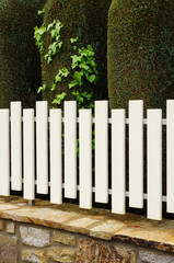 PVC-Zaun auf Natursteinmauer vor Zypressenhecke
