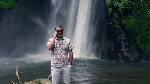 Man talking on cellphone next to waterfall, slow motion 240fps
