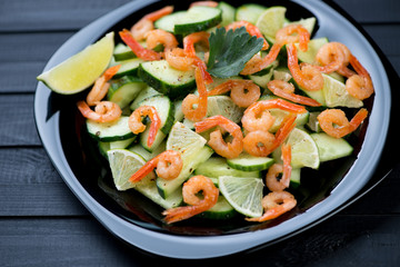 Salad with shrimps, cucumbers and lime in a black glass plate