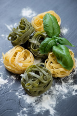 Raw tagliatelle with green basil and flour, black wooden surface