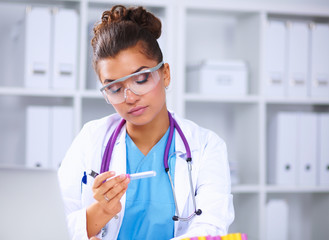Woman researcher is surrounded by medical vials and flasks, iso