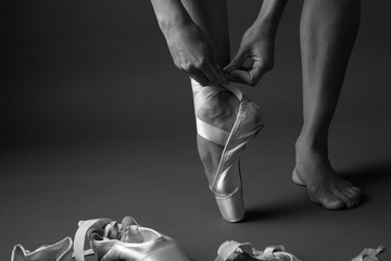 Feet of ballerina tying ribbons of pointe, monochrome