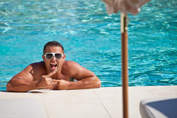 Young wet sexy muscular man posing in the swimming pool