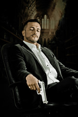 Elegant man sitting in a chair holding  gun over dark background