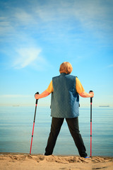 active woman senior nordic walking on a beach. from behind