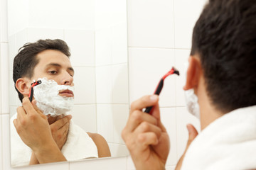 Young man shaving his beard with razor at the bathroom