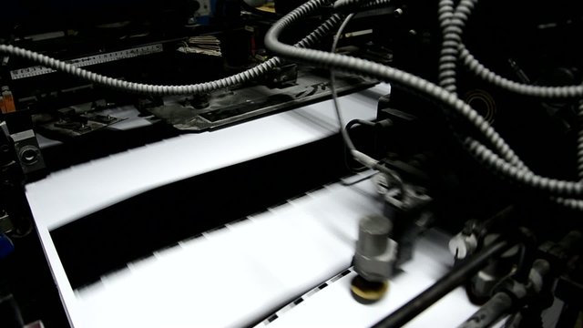 Sheet pages being fed into a four color offset printing press.