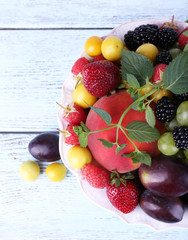 Different berries and fruits in plate on wooden table close-up