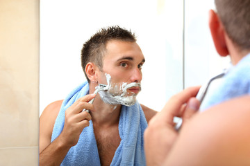 Young man shaving his beard in bathroom