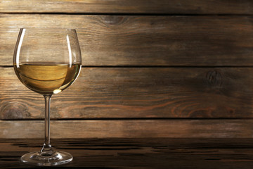Goblet of white wine on wooden table on wooden wall background