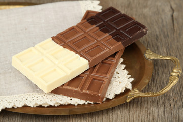 Chocolate bars on napkin, on tray, on wooden background