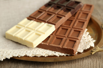 Chocolate bars on napkin, on tray, on wooden background