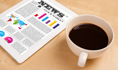 Tablet pc shows news on screen with a cup of coffee on a desk