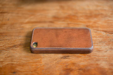 iphone with genuine leather cover on the wooden table.