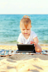 Happy baby with tablet pc on beach.