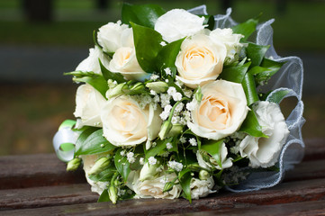 Wedding bouquet of cream roses and green leaves on wooden bench