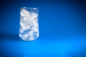 A glass of ice cubes on blue background