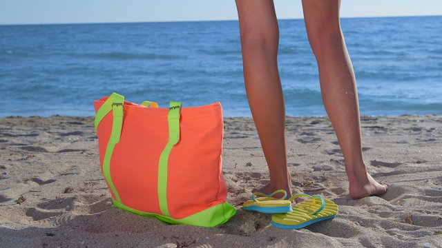 Colorful bag and flip-flops on sandy beach bikini woman